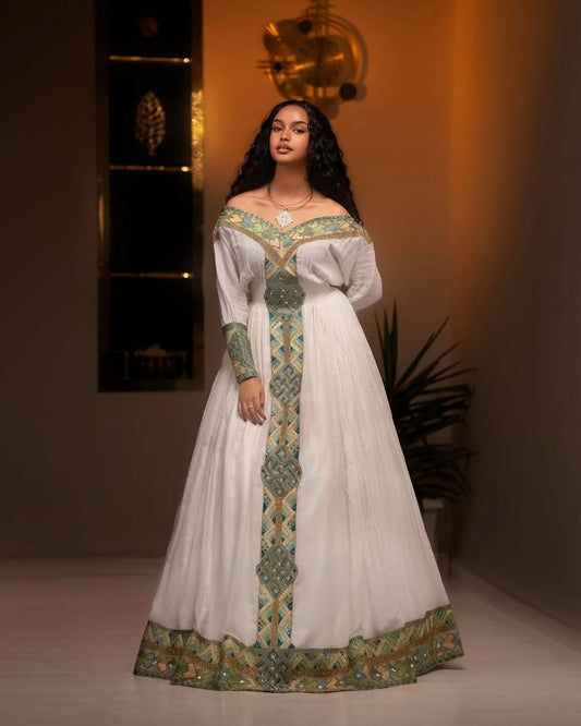 Woman wearing a white and green traditional Ethiopian libs with intricate patterns in a warm-toned room.