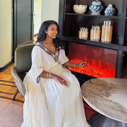 Woman in a white Ethiopian Dress  sitting in front of a modern fireplace.