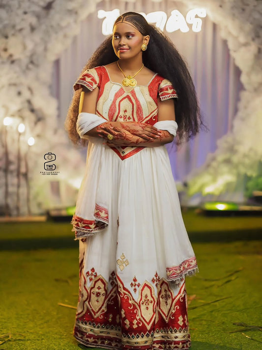 Woman in a traditional red and white Habesha outfit with intricate patterns, standing outdoors.