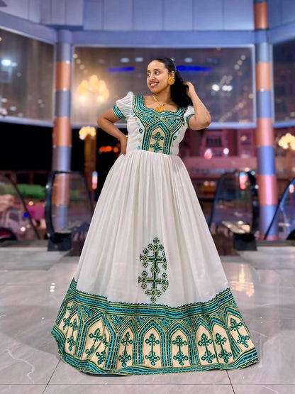 Woman wearing a white Ethiopian Dress with green embroidery in an indoor setting