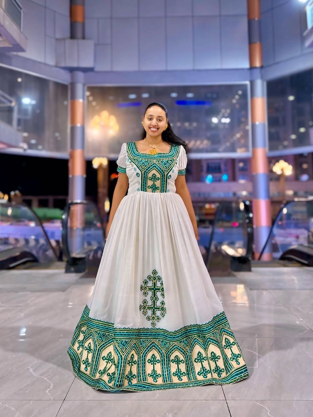 Woman wearing a white Ethiopian Dress with green embroidery in an indoor setting