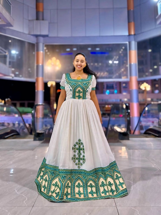 Woman wearing a white Ethiopian Dress with green embroidery in an indoor setting