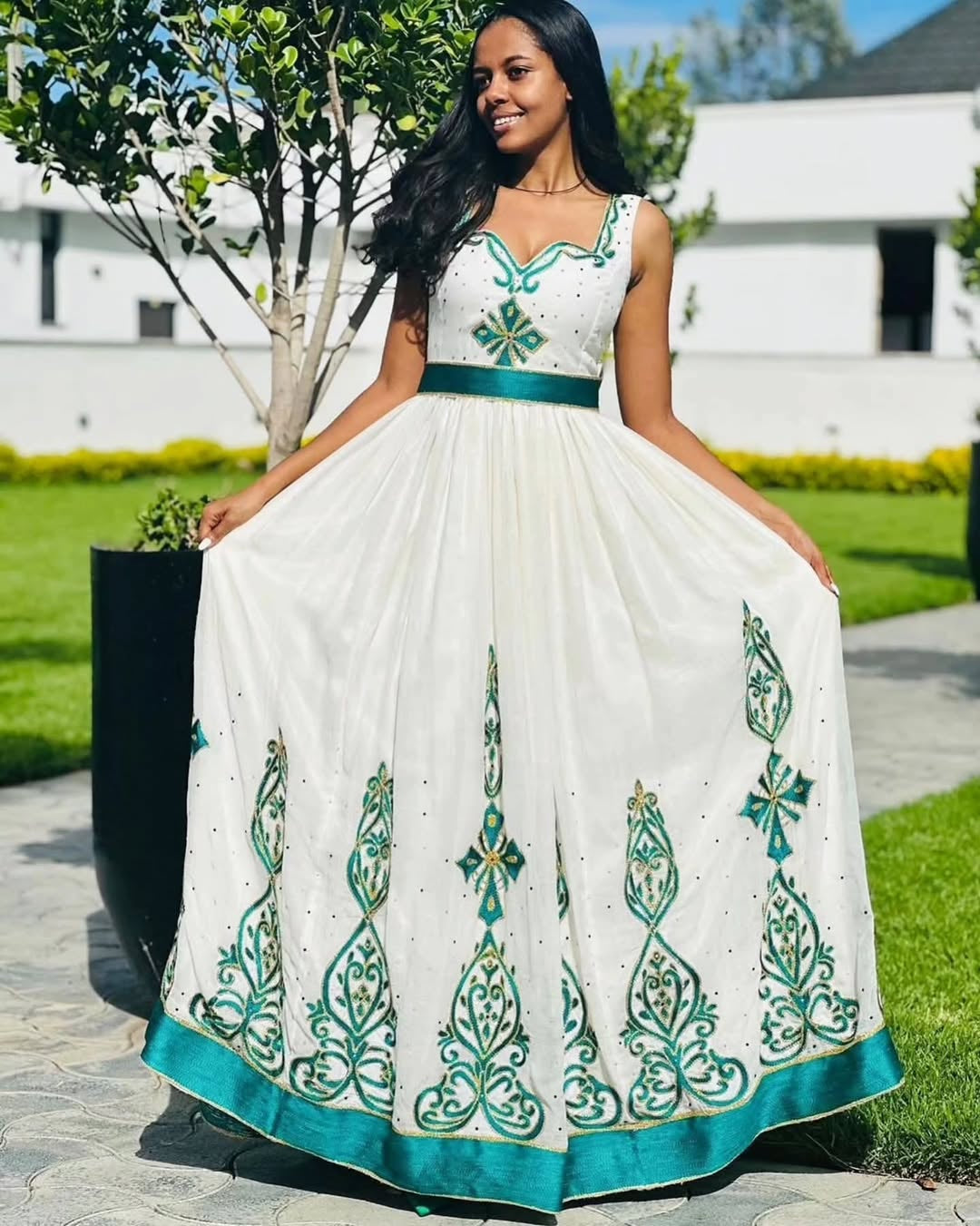 Woman wearing a white Habesha Dress with green embroidery in an outdoor setting