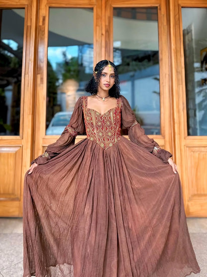 Woman in a long brown Ethiopian traditional dress standing in front of wooden doors.