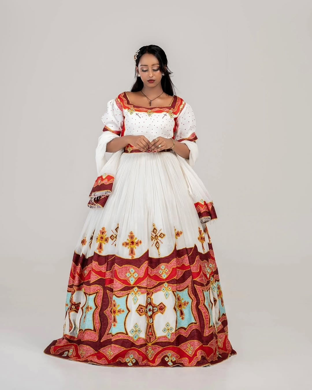 Woman wearing a traditional habesha dress with intricate patterns on a plain background