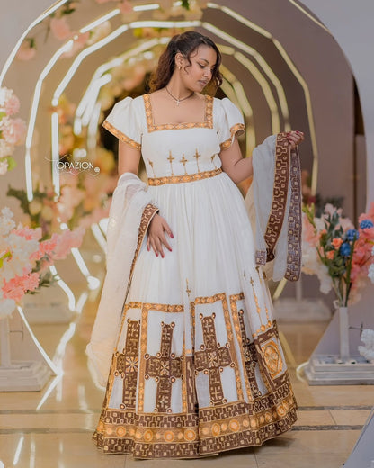 Woman in a white and gold Ethiopian Traditional Wedding Dress standing in a decorated indoor setting.