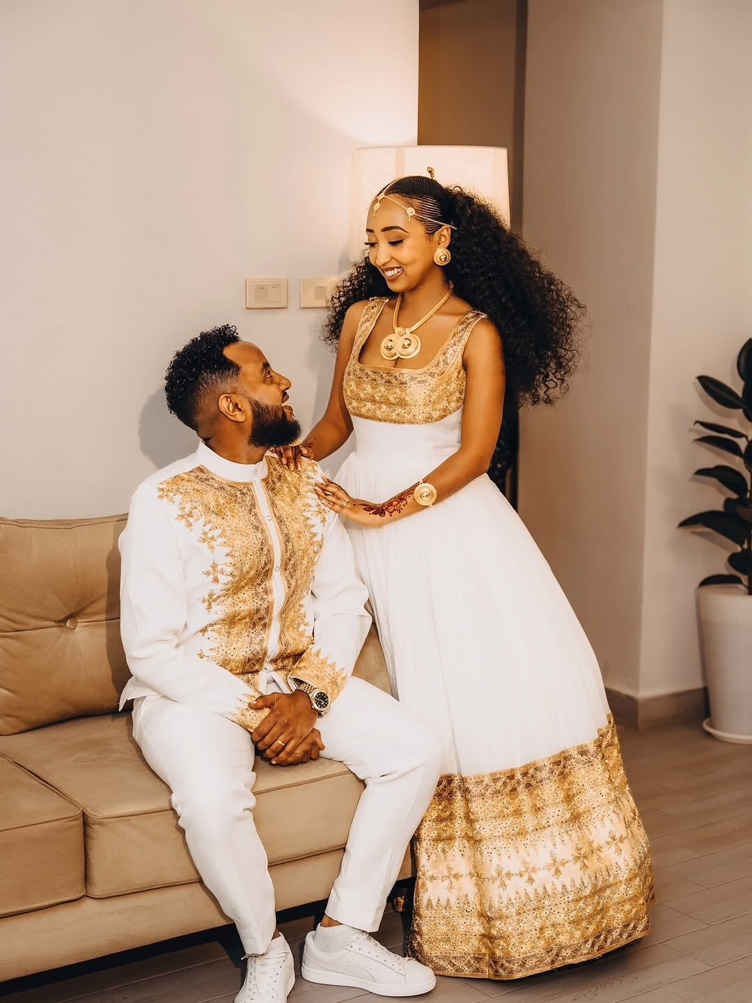 Couple in formal Gold Ethiopian Matching Couple Wedding Set sitting on a couch in a living room.