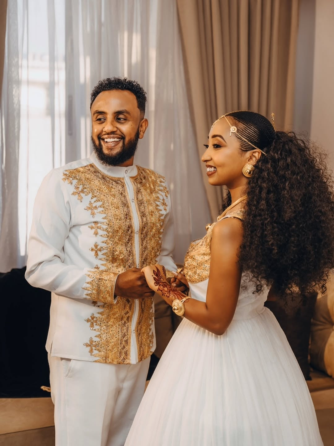 Man and woman in formal Gold Ethiopian Matching Couple Wedding Set standing close together indoors.