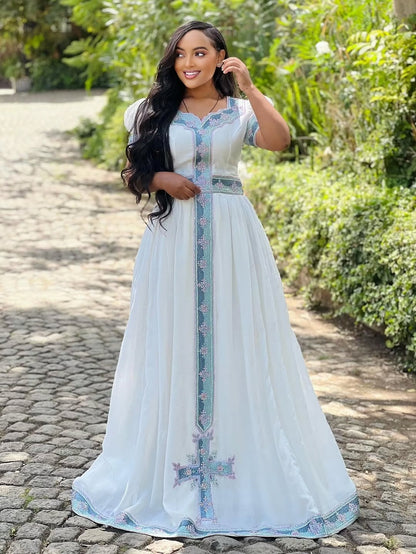 Woman in a long, light blue Ethiopian dress with floral patterns standing on a stone path.