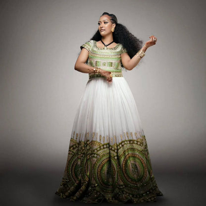 A woman modeling a traditional African Habesha Wedding Dress  with a green and white patterned bodice and a voluminous white skirt featuring a green and gold circular pattern at the hem, set against a dark gray studio background.