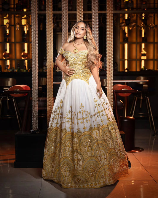 A woman modeling an off-the-shoulder white and gold ball Ethiopian Dress for Women in a dimly lit, upscale indoor venue with warm ambient lighting.