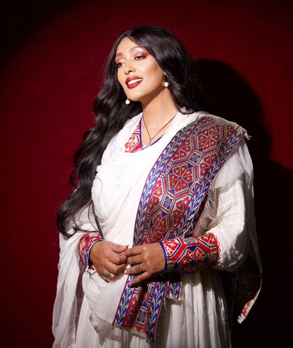 Woman wearing a Ethiopian Habesha Dress with a red and blue pattern against a dark background
