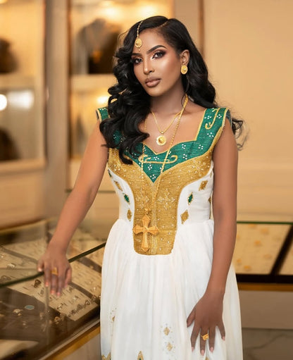 Woman wearing a gold and green traditional Green Habesha Kemis with jewelry in an indoor setting.