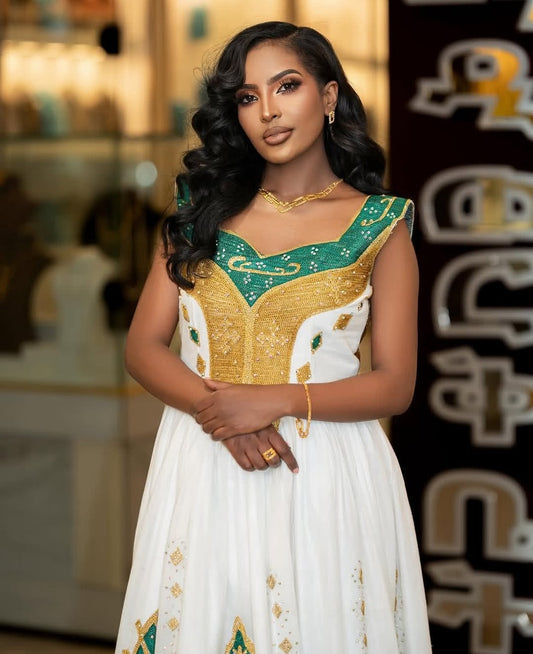 Woman in a white and gold Green Habesha Kemis with green accents, standing in front of a decorative background.