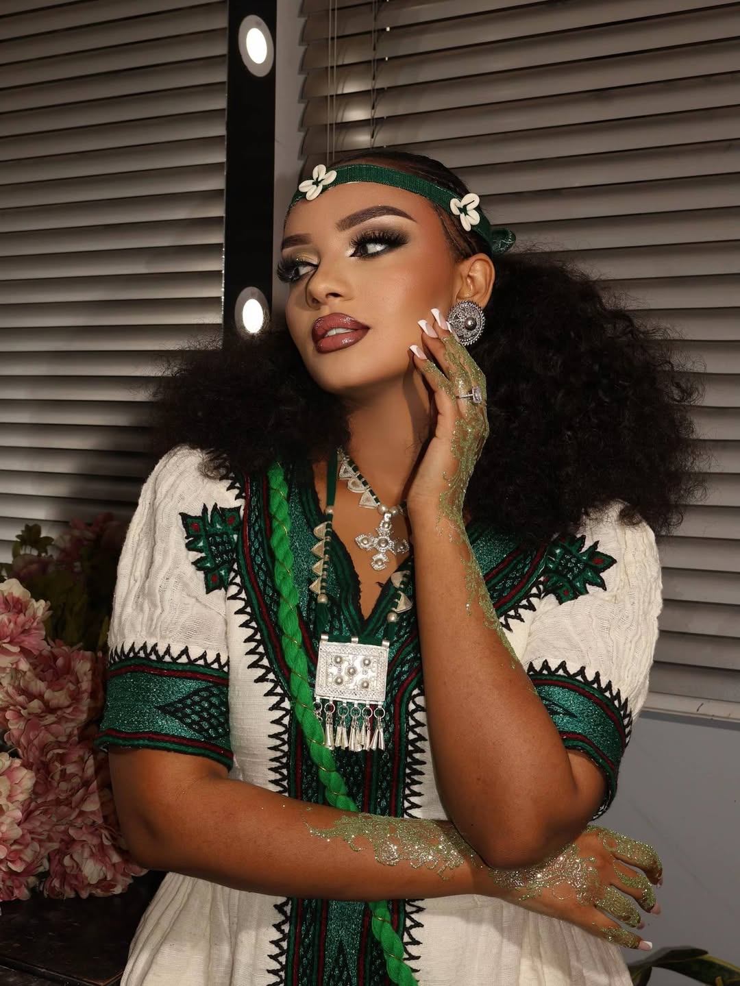 Woman in Ethiopian traditional dress with jewelry and floral headband against a neutral background