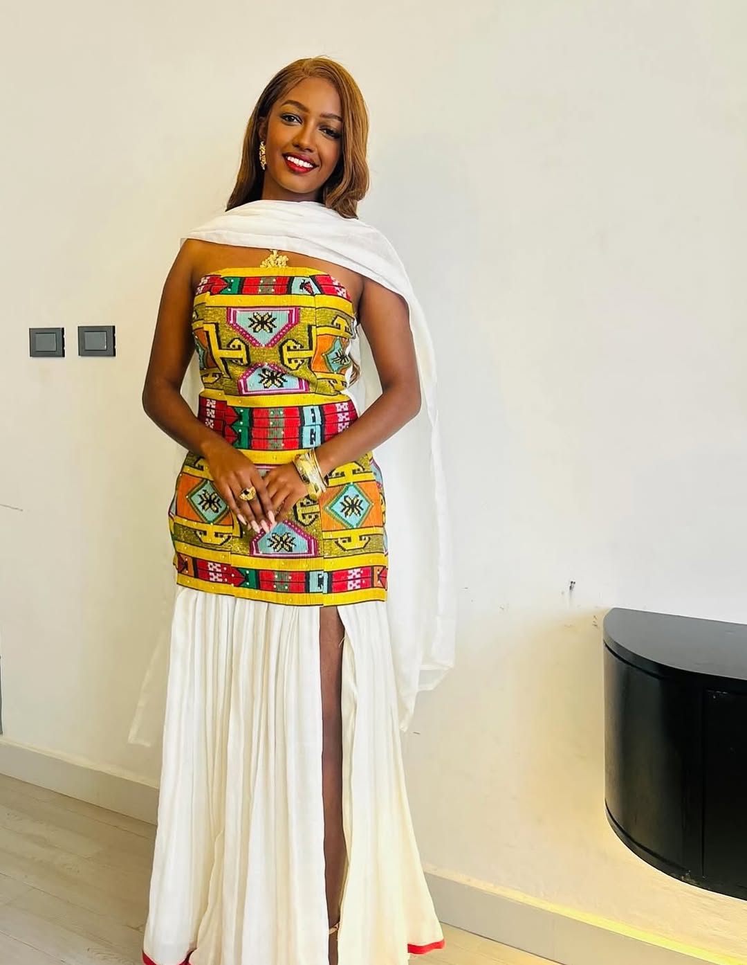 Woman wearing a colorful Ethiopian traditional dress with a white overlay in an indoor setting