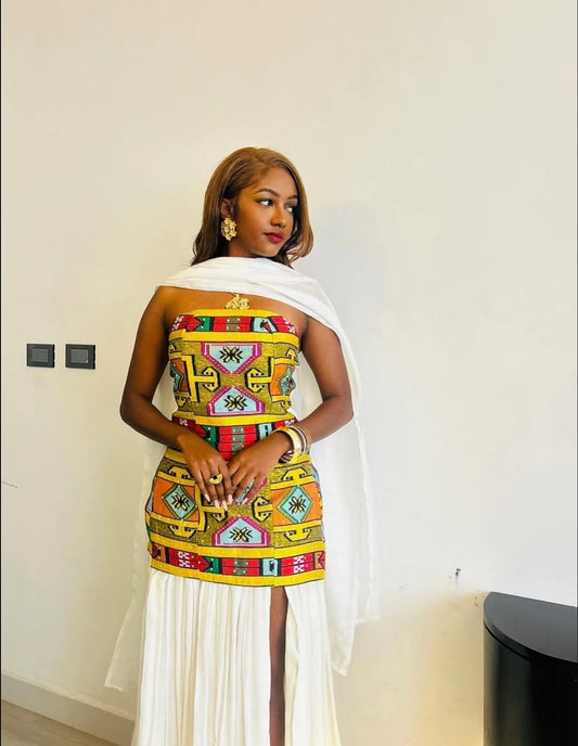 Woman wearing a colorful Ethiopian traditional dress with a white overlay in an indoor setting.