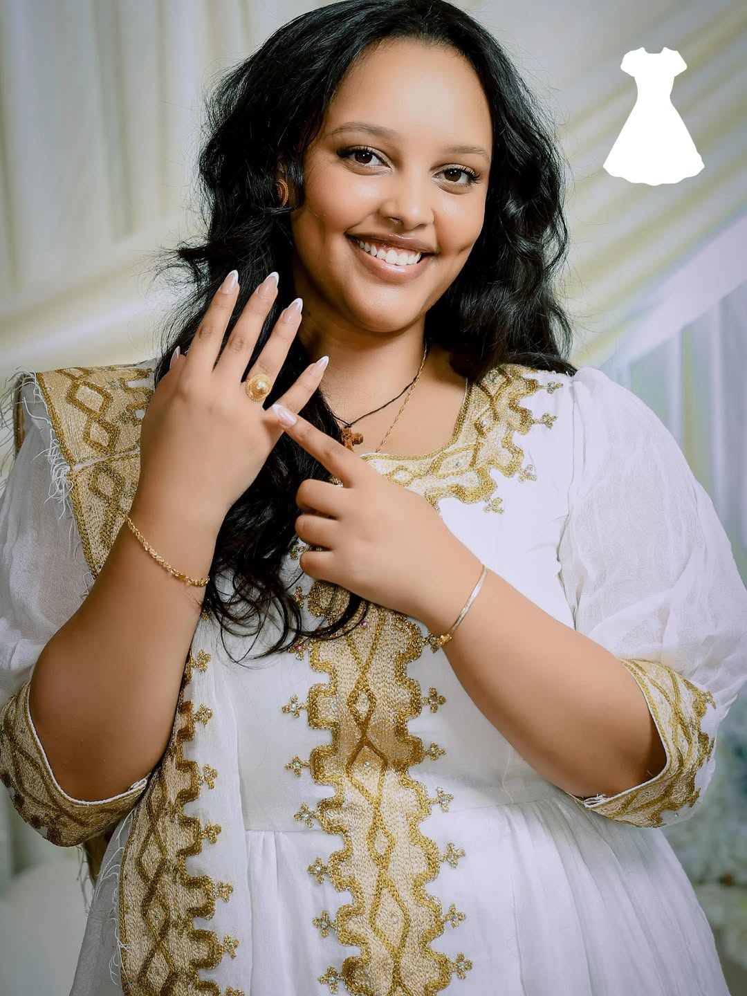 Woman in a white and gold embroidered Ethiopian traditional dress showing off a ring.