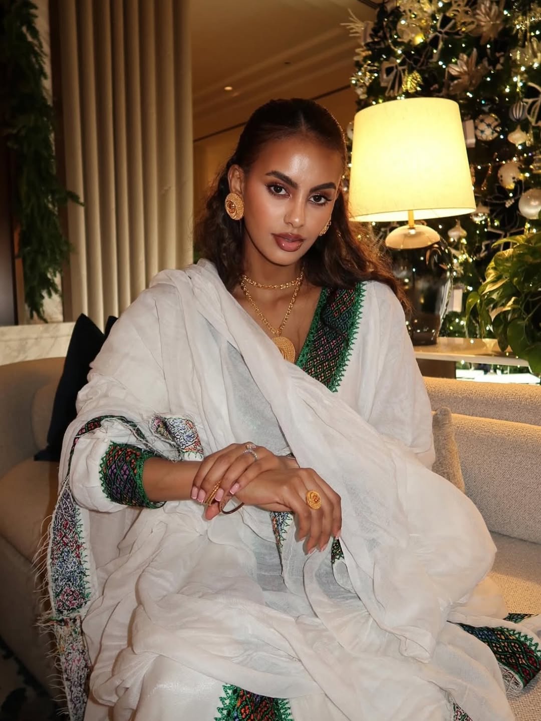 Woman in a white and green traditional Ethiopian traditional dress sitting in a decorated room with a Christmas tree.