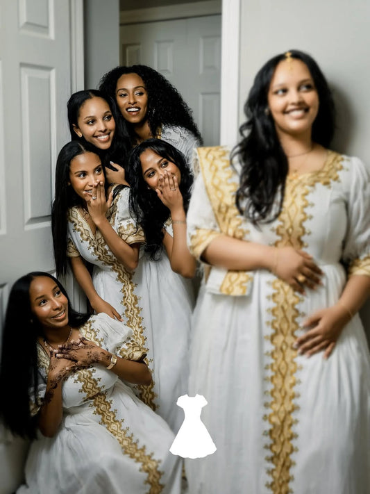 Group of women in white Ethiopian traditional dress with gold accents posing together indoors.