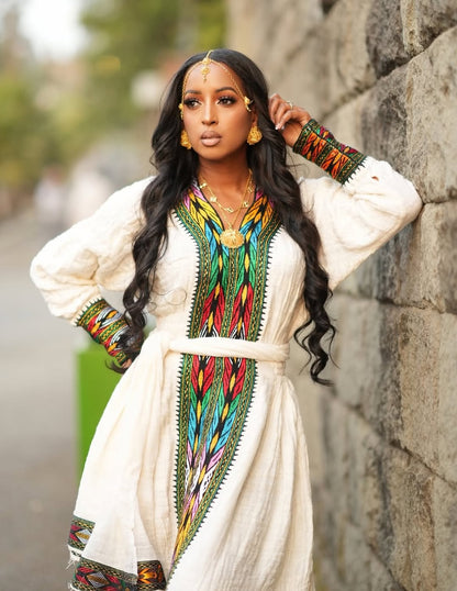 Woman in a Ethiopian traditional outfit with colorful patterns leaning against a stone wall.