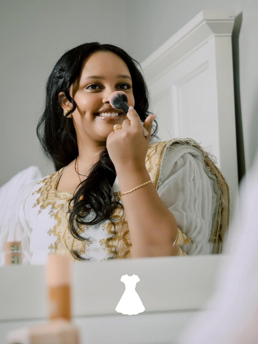 Woman applying makeup in front of a mirror dressing Ethiopian traditional dress 