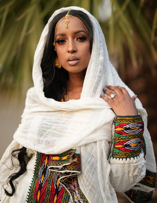 Woman wearing a white headscarf and colorful Ethiopian traditional dress with a blurred natural background