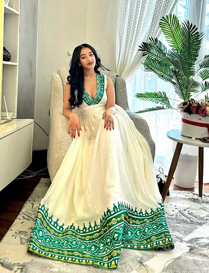 Woman in a white and green Ethiopia traditional dress sitting on a chair in a modern living room.