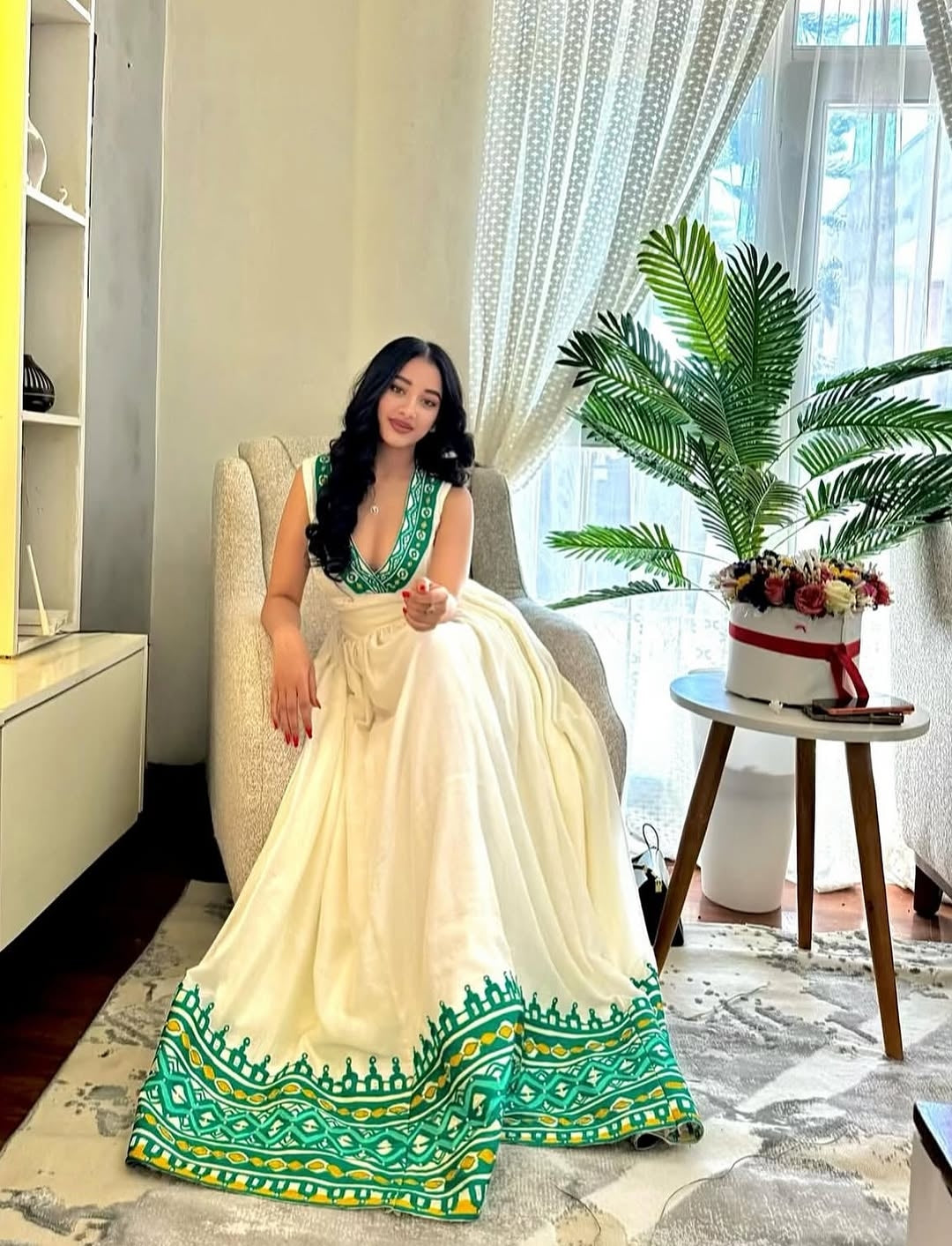 Woman in a white and green Ethiopia traditional dress sitting in a modern living room.