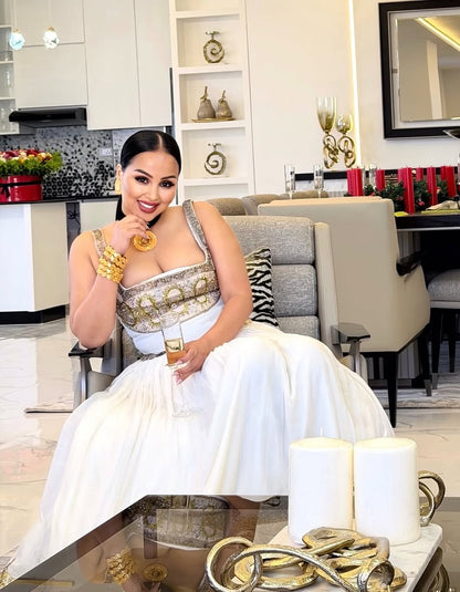 Woman in a white and gold Ethiopia traditional dress sitting in a modern living room.