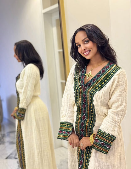 Woman wearing a traditional Ethiopian traditional dress with intricate patterns in a room.