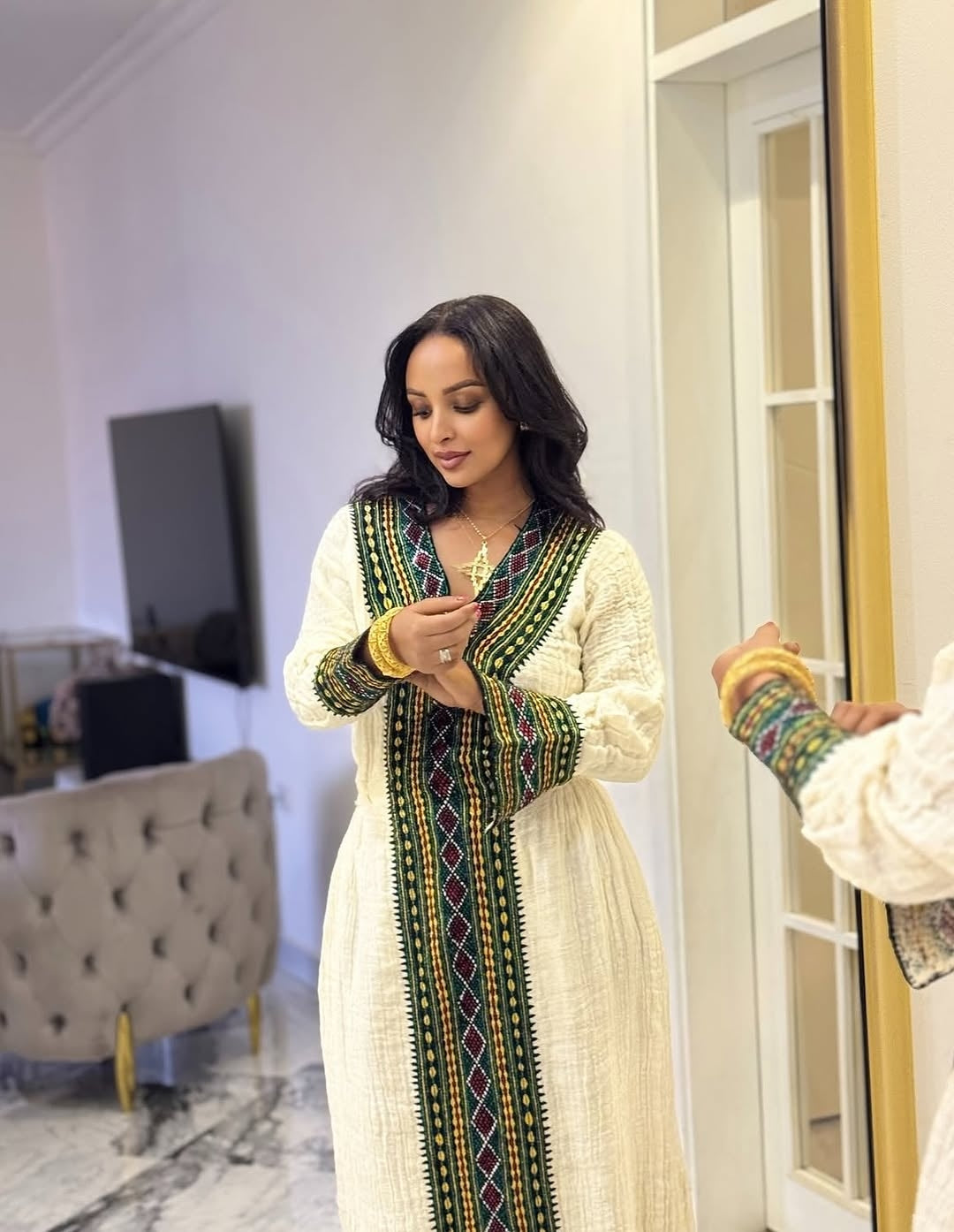 Woman wearing a traditional Ethiopian traditional dress with intricate patterns in a room.