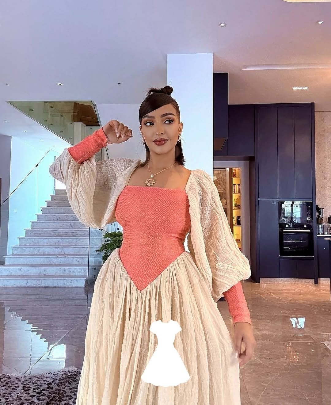 Woman in a peach top and beige Ethiopian traditional dress standing in a modern kitchen.