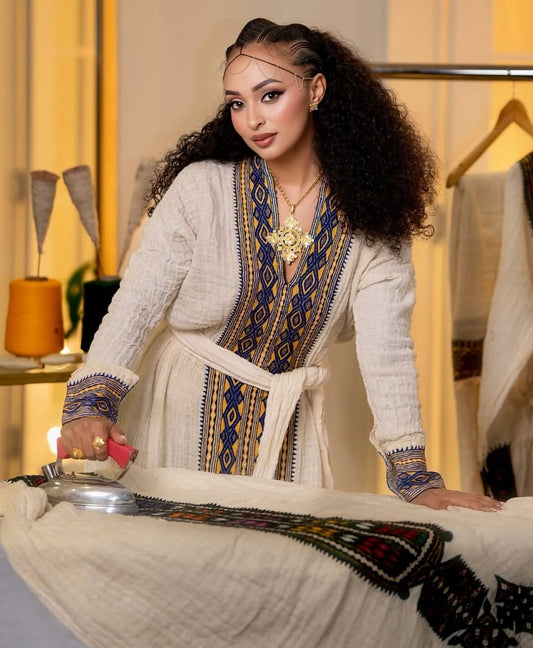 Woman in 
embroidered Eritrean Dress
 outfit in a room with decor elements.