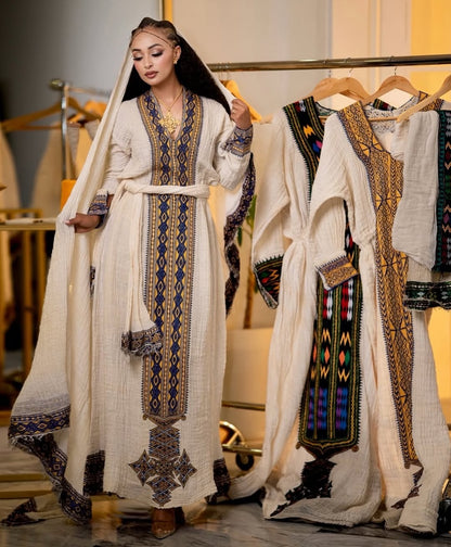 Woman in traditional embroidered Eritrean Dress standing next to a rack of similar dresses.