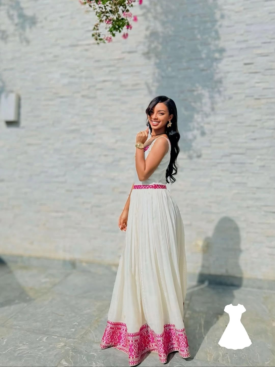 Woman in a white and pink Ethiopian Kemis
 standing against a light stone wall.