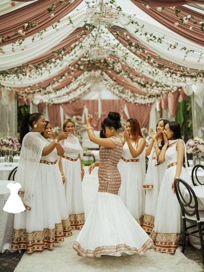 Woman in a white and gold Habesha Wedding Dress dancing in a decorated indoor setting with floral arrangements.