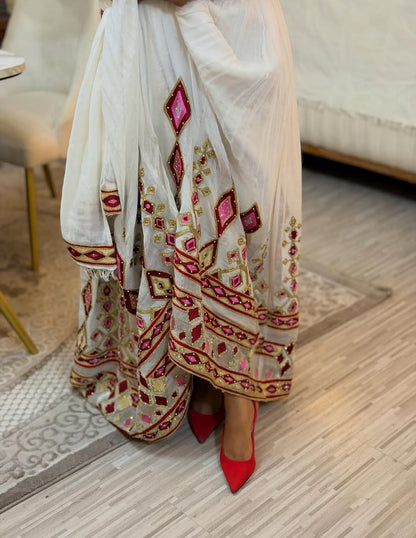 White saree with red and gold Ethiopian Libs embroidery on a wooden floor.