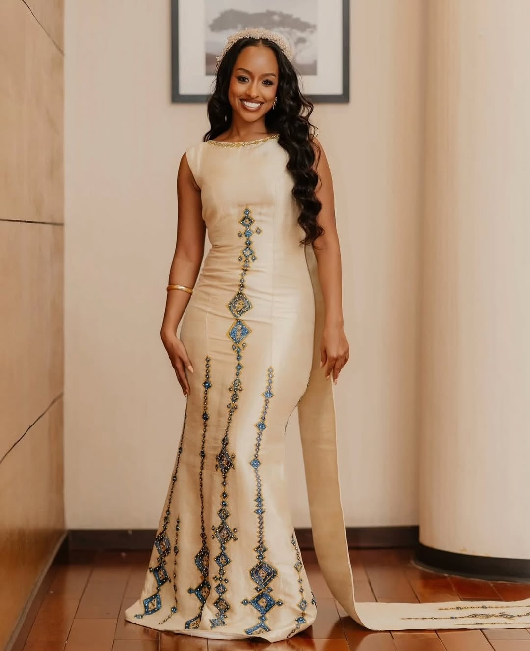 Woman in a long, elegant Habesha Kemis with decorative elements standing indoors.