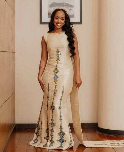Woman in a long, elegant Habesha Kemis with decorative elements standing indoors.