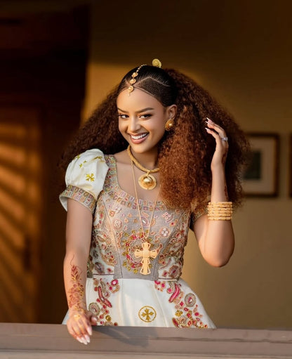 Woman in Ethiopian Wedding Dress attire with jewelry, smiling outdoors.