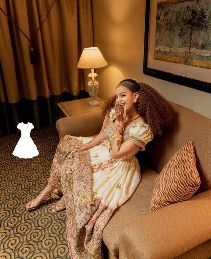 Woman in a Ethiopian Wedding Dress outfit sitting on a couch in a room with a lamp and painting.