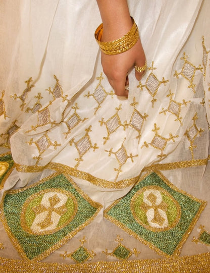 Close-up of a white fabric with gold and green Red Ethiopian Wedding Matching Set, featuring a hand wearing a gold bracelet.