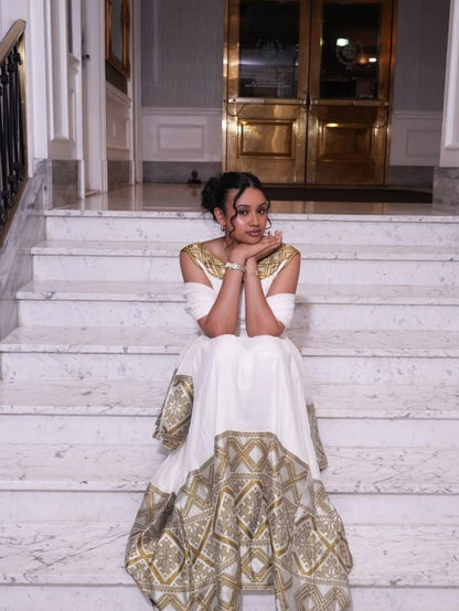 Woman in a white and gold Habesha Kemis sitting on marble steps.