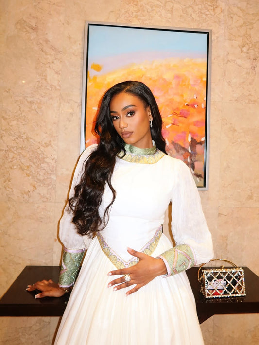 Woman in a white and green Habesha Dress standing in front of a colorful abstract painting.
