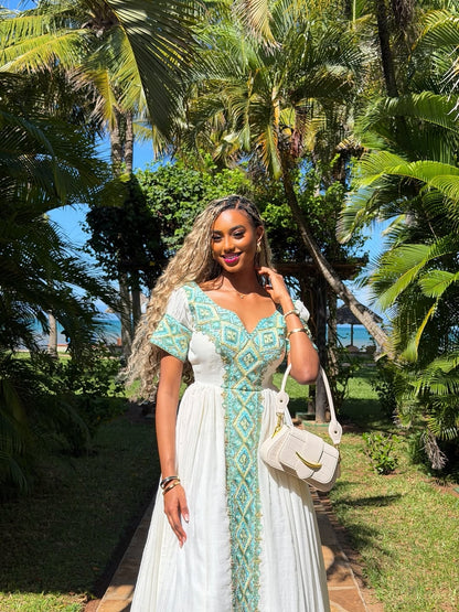 Woman in a white and green dress standing in a tropical setting with palm trees.
