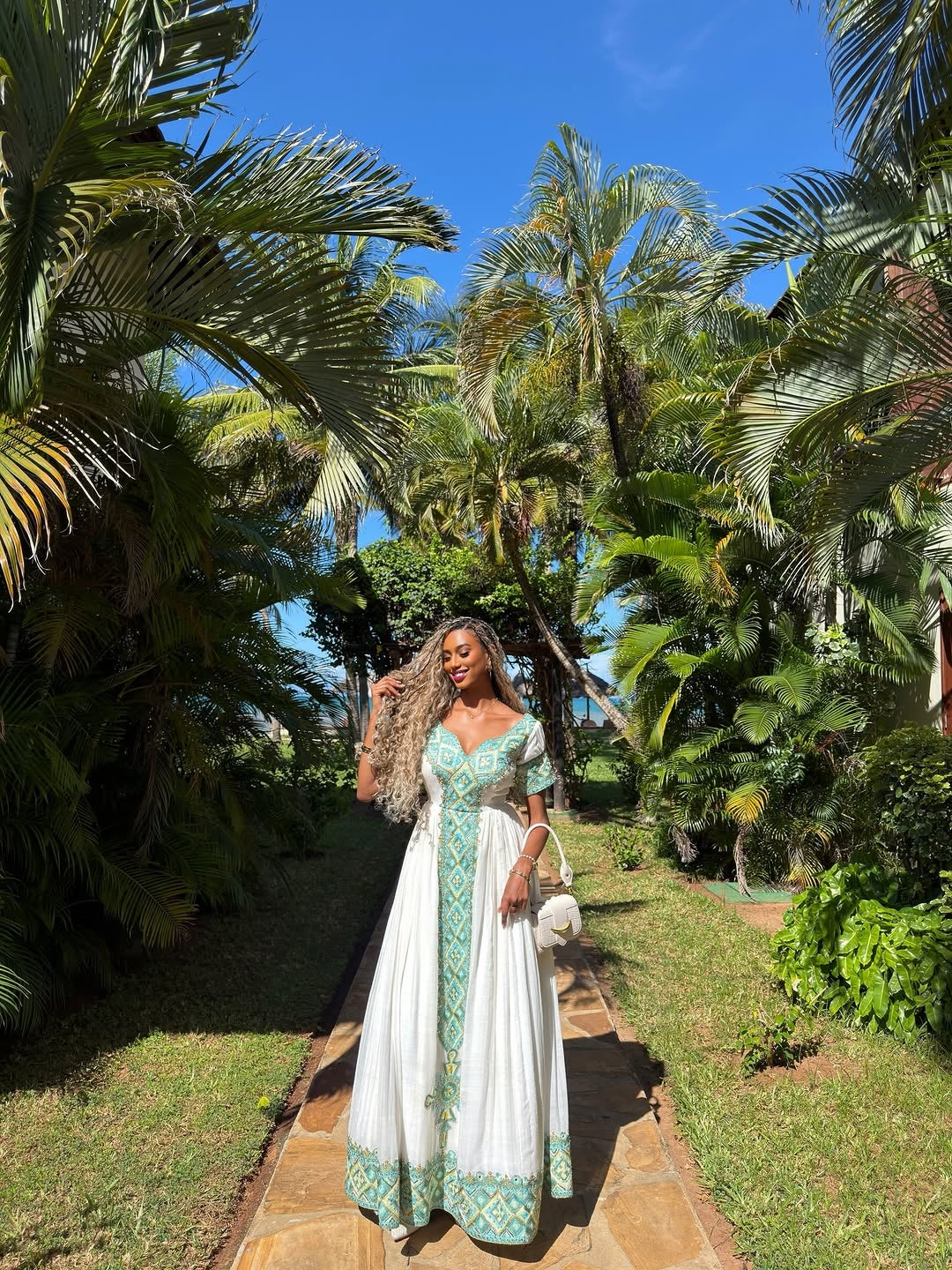 Woman in a green and white Green Eritrean Libs standing in a tropical garden with palm trees.