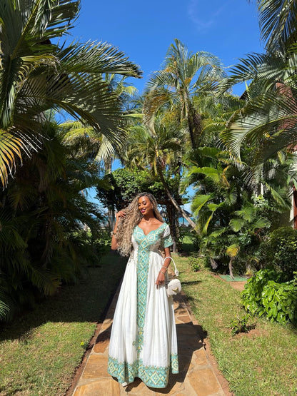 Woman in a green and white Green Eritrean Libs standing in a tropical garden with palm trees.