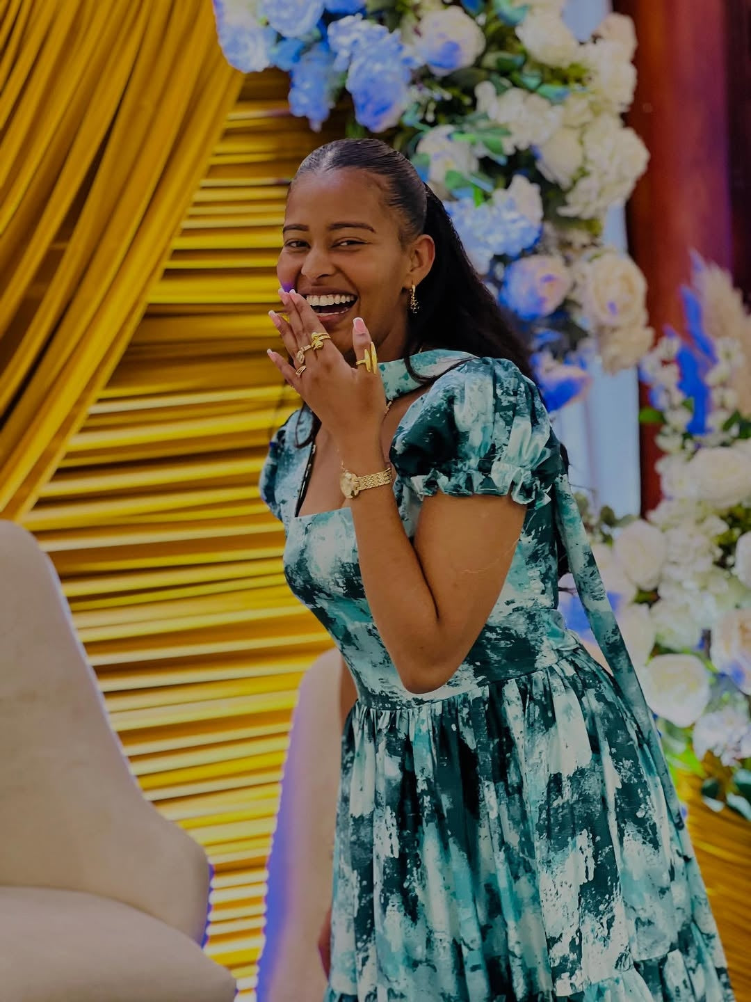Woman in a Green Habesha Chiffon laughing in front of a decorated backdrop with flowers and yellow elements.