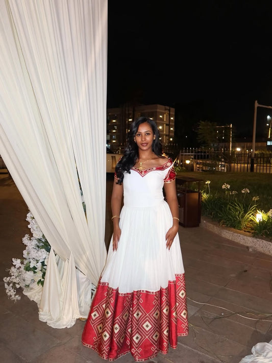Woman in a white and red Ethiopian Libs standing next to a white curtain at night.